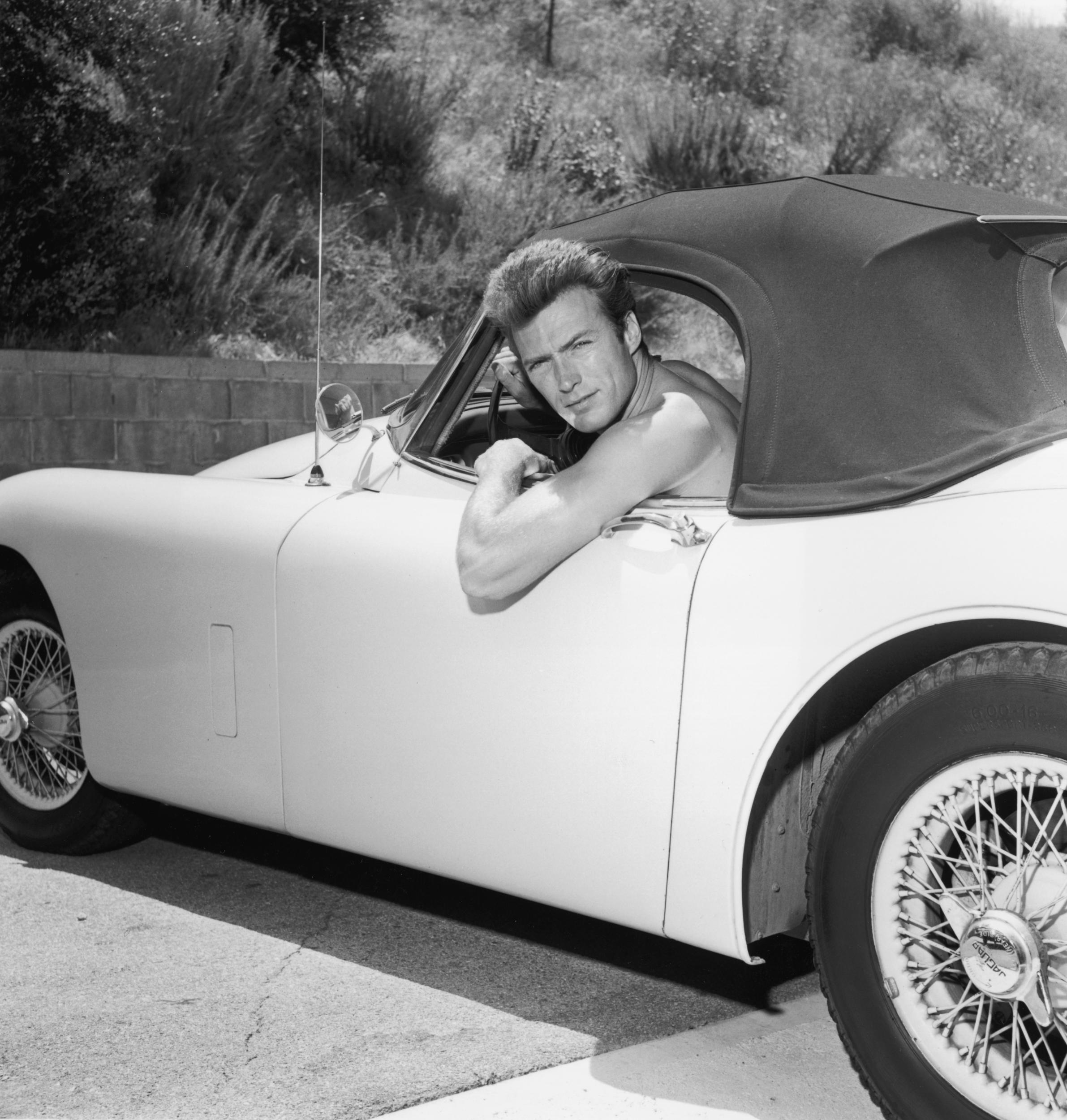 Small car for a big guy. A shirtless Clint Eastwood strikes a pose with his Jaguar convertible, circa 1965. 