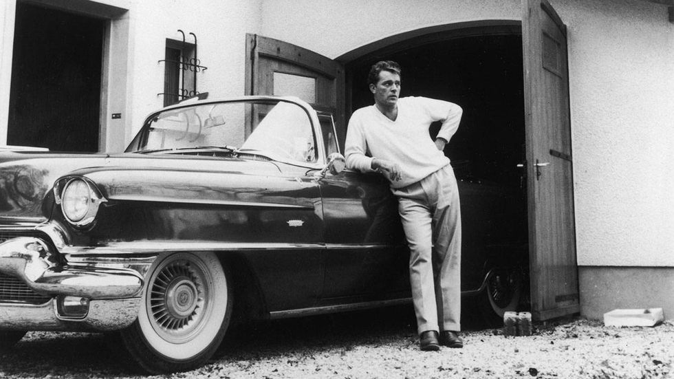 Welsh actor Richard Burton (1925-1984) stands next to a Cadillac and garage.