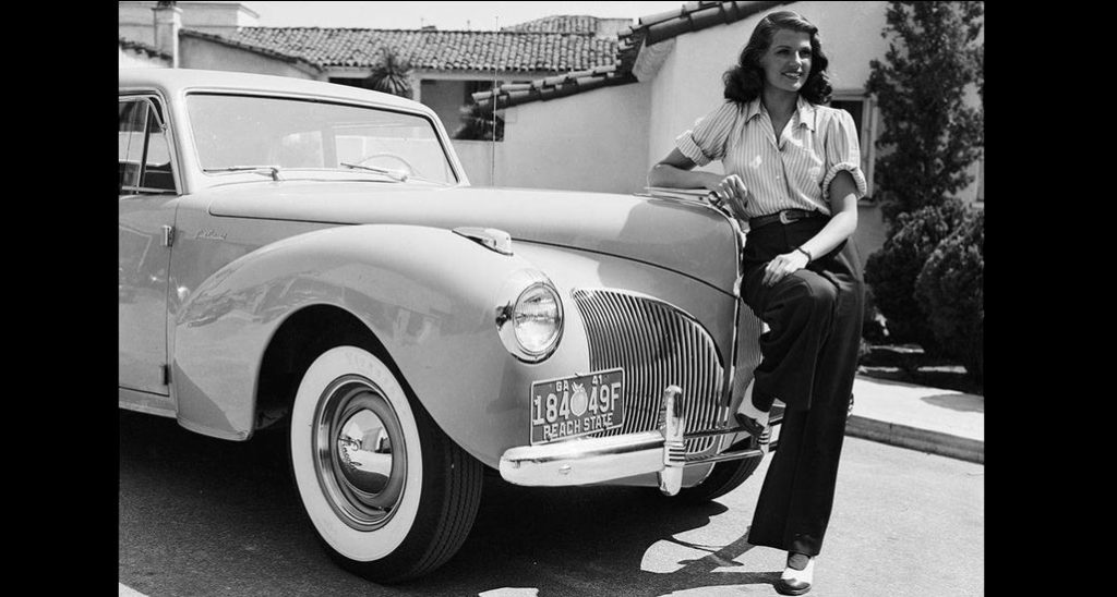 1941: American screen beauty Rita Hayworth poses beside a Lincoln.