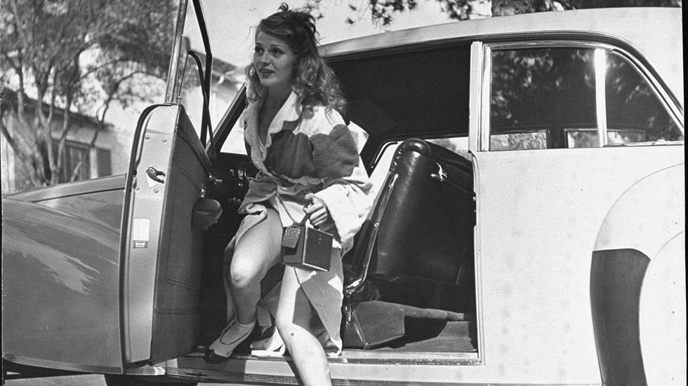 Rita Hayworth Actress Rita Hayworth clad in bathrobe over her swimsuit as she steps out front driver's side of her car in driveway at home after a day at the beach.